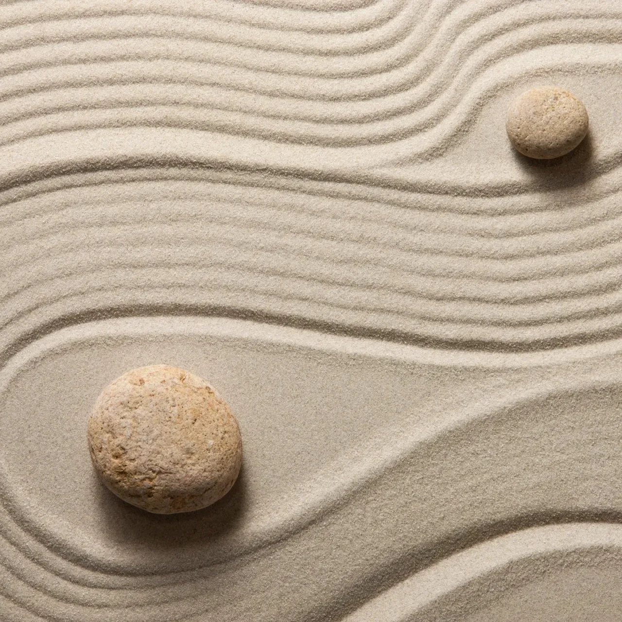 Two stones are sitting on a sand pattern.